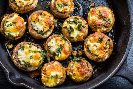 Baked champignons mushrooms, filled with cheese, parsley and roasted garlic in black bowl. Selective focus. Healthy food concept.の写真素材