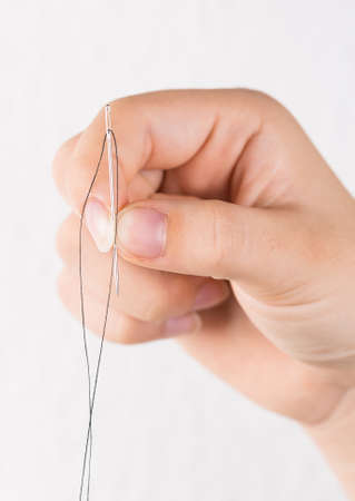 Detail of hand holding needle with thread on white backgroundの写真素材