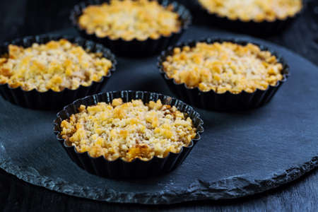 Small and delicious apple pies or apple crumble on black background. Appel tart.の写真素材
