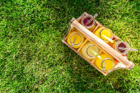 Assortment of lemonade and ice tea in bottles in wooden rack in the grassの写真素材