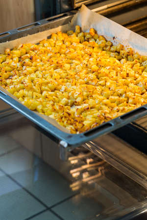 Baking tray with golden roasted potatoes in the open ovenの写真素材