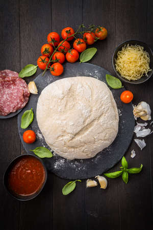 Fresh raw dough for pizza with ingredients and spices on wooden table. Concept of homemade cooking.の写真素材