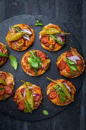 Homemade small pizza with pesto, salami, tomatoes and arugula on black backgroundの写真素材