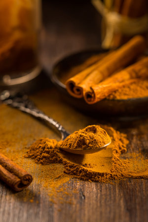Cinnamon powder in vintage spoon with cinnamon sticks on wooden background as cooking and baking...