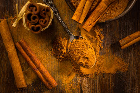 Cinnamon powder in vintage spoon with cinnamon sticks on wooden background as cooking and baking ingredient.の写真素材
