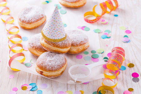Traditional Berliner with party hat for carnival and party. German Krapfen or donuts with streamers and confetti. Colorful carnival or birthday imageの写真素材