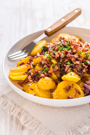 German fries - fried potatoes with bacon and onion topping on plateの写真素材