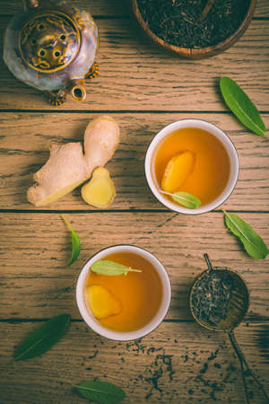 Ginger tea with sage leaves and dried black tea leaves on wooden backgroundの写真素材