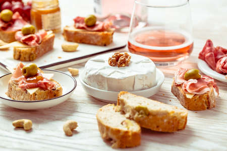 Appetizers and open sandwiches with Italian antipasti, camembert, Parma ham and rose wine on wooden tableの写真素材