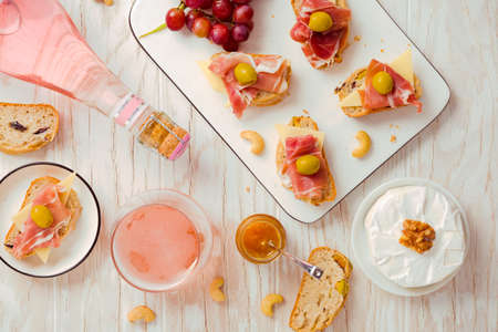 Flat lay of  Appetizers and open sandwiches with Italian antipasti, camembert, Parma ham and rose wine on wooden tableの写真素材