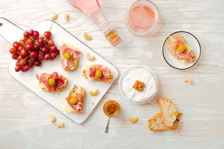 Flat lay of  Appetizers and open sandwiches with Italian antipasti, camembert, Parma ham and rose wine on wooden tableの写真素材