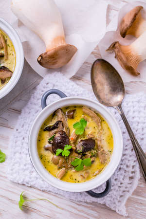 Delicious mushroom soup with herbs in serving pot on wooden tableの写真素材