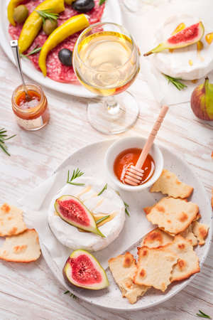 Camembert with honey, fig with antipasti and glass of white wine on wooden backgroundの写真素材