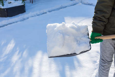 Child shoveling and removing snow in front of his house in the suburbの写真素材