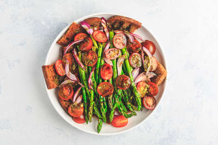 Warm green asparagus salad with tomato, onion and roaster bread.の写真素材