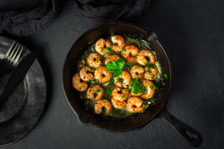 Shrimps with garlic, olive oil and parsley in frypan on black backgroundの写真素材