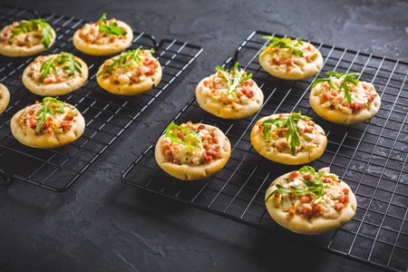 Small tarte flambee or mini pizza with onion, bacon and arugula on black backgroundの写真素材