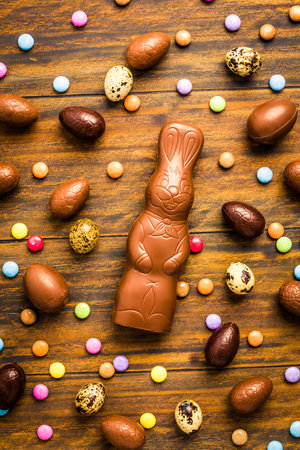 Chocolate Easter bunny with sweet chocolate eggs and colorful sweets on wooden backgroundの写真素材