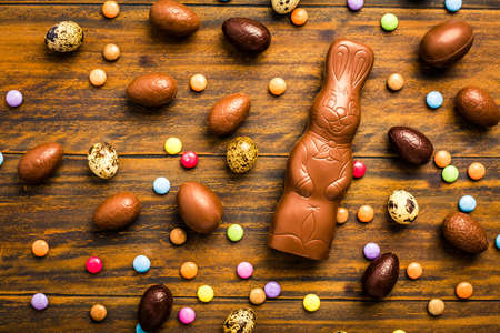 Chocolate Easter bunny with sweet chocolate eggs and colorful sweets on wooden backgroundの写真素材