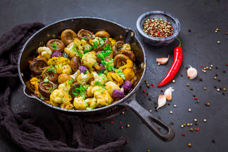 Roasted mushrooms and cauliflower, with onion, garlic and herbs in pan on black backgroundの写真素材
