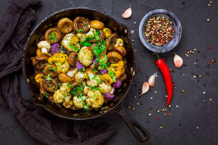 Roasted mushrooms and cauliflower, with onion, garlic and herbs in pan on black backgroundの写真素材