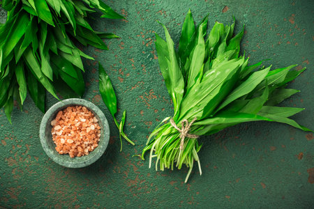 Bunch of Ramson or bear leek (Allium ursinum) with pink Himalayan salt on kitchen table.