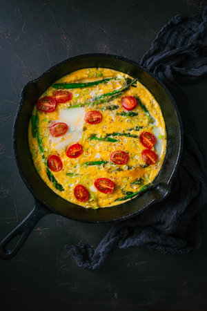 Delicious fritatta with green asparagus and cherry tomatoes in pan