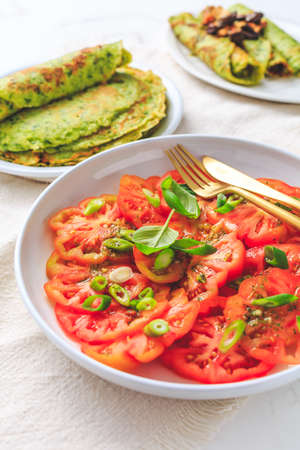 Tomato salad with onions and ramson pancakes or crepes on white backgroundの写真素材