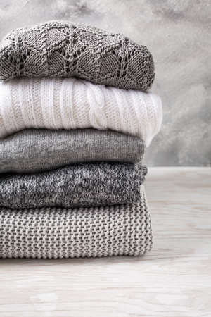 Stack of cozy knitted sweaters and pullovers on wooden background. Autumn and winter conceptの写真素材