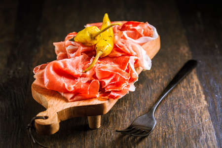 Prosciutto with grilled peppers -  Italian dry ham with grilled green peppers on wooden tableの写真素材