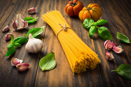 Ingredients for mediterranean pasta dish - spaghetti, tomatoes, basil, pepper, garlic on wooden background.の写真素材