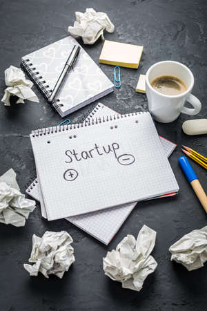 Startup concept - Notepad, coffee, discarded ideas and writing tools on black deskの写真素材