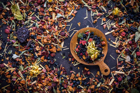 Dried tea leaves, fruits and berries in bowl on rustic wooden tableの写真素材