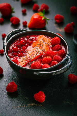 Breakfast red smoothie bowl with chia seeds, strawberry, raspberry and redcurrants on black backgroundの写真素材
