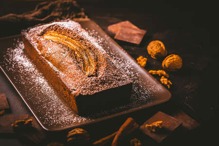Homemade vegan banana bread or cake with nuts, chocolate and cinnamon on brown backgroundの写真素材