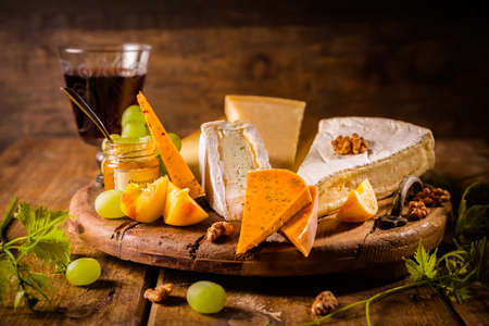 Cheese platter, assortment of different cheeses with glass of red wine, grapes on wooden tableの写真素材
