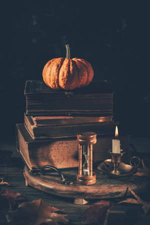 Still life for Halloween and Thanksgiving with old books, pumpkins and candle on dark background