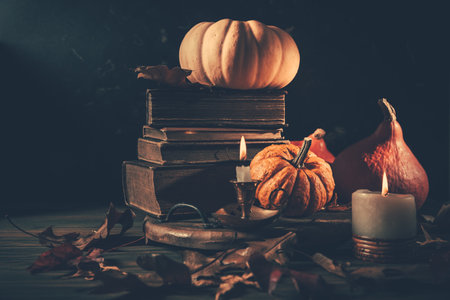 Still life for Halloween and Thanksgiving with old books, pumpkins and candle on dark backgroundの写真素材