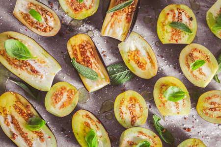 Small raw eggplants prepared for baking on baking sheet with herbs and spicesの写真素材