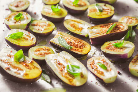 Small raw eggplants prepared for baking on baking sheet with herbs and spicesの写真素材