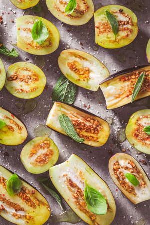 Small raw eggplants prepared for baking on baking sheet with herbs and spicesの写真素材