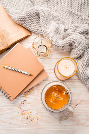 Hot herbal tea with notepad, candle, book and blanket. Cozy and hygge lifestyleの写真素材
