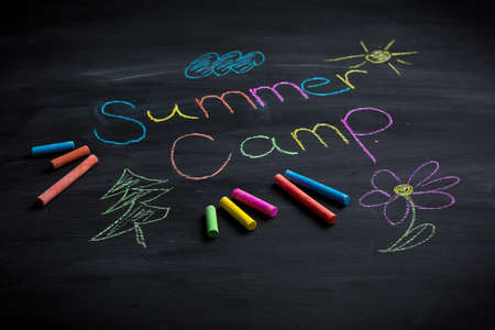 Text Summer camp written on black chalkboard, with chalk sticks of different colorsの写真素材