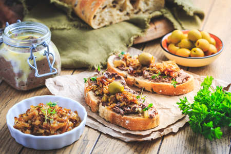 Fresh homemade chicken liver pate on ciabatta bread with roasted onions and olives on wooden tableの写真素材
