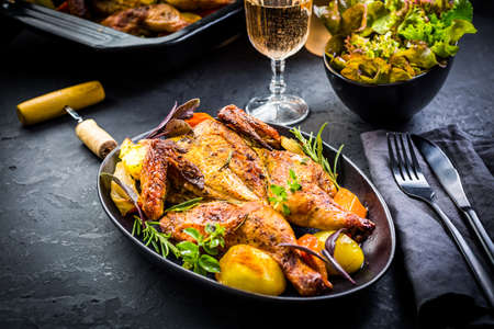 Baked whole chicken with potatoes, carrots, herbs and salt and rose wine on black backgroundの写真素材