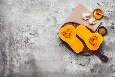 Halves of raw organic butternut squash with spices and ingredients for cookingの写真素材