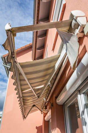 Old, messy, dirty and broken retractable awning installed on family house