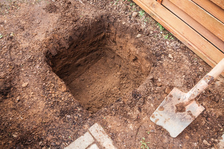 Hole in a soil, prepared for planting or construction, pit in a ground with shovelの写真素材