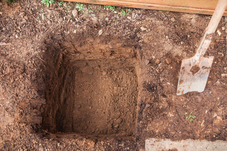 Hole in a soil, prepared for planting or construction, pit in a ground with shovelの写真素材