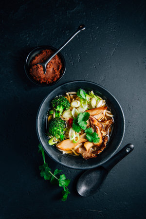 Vegan miso or ramen soup with mushrooms and vegetables on black background